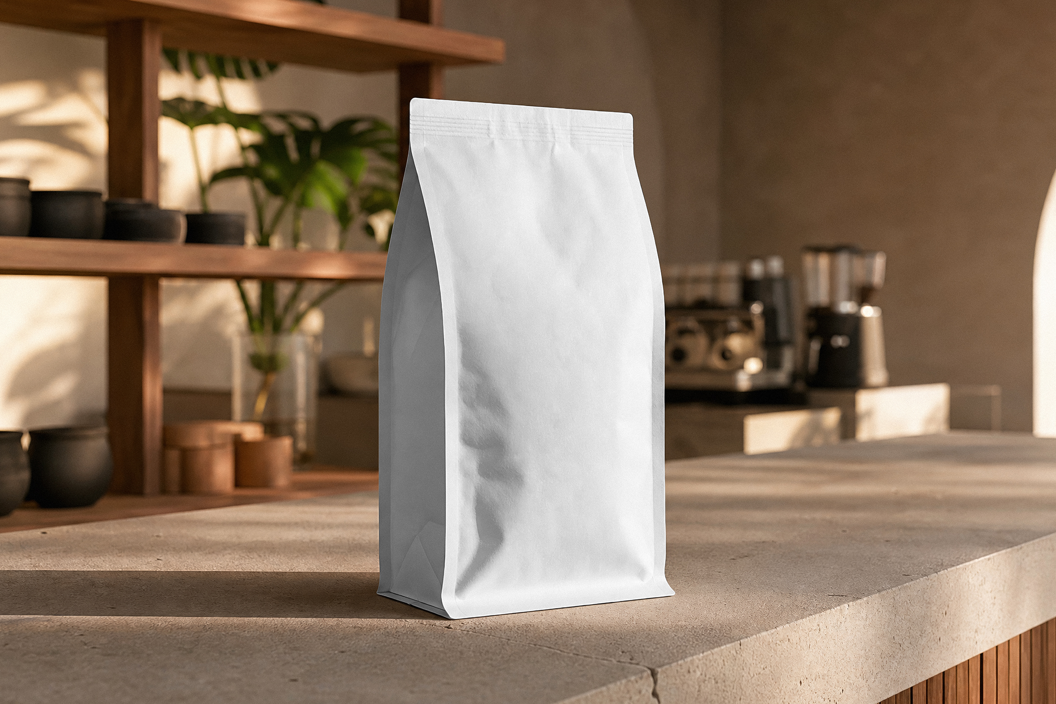 A blank white stand-up coffee pouch standing on a stone countertop in a cozy, sunlit café setting with wooden shelves in the background.