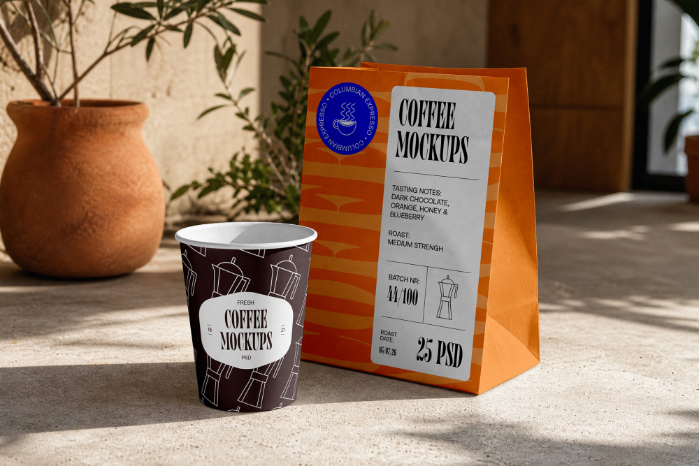 A dark brown paper coffee cup featuring a white Moka pot pattern placed next to a tall orange paper takeaway bag on a concrete floor.