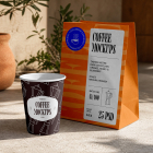 A dark brown paper coffee cup featuring a white Moka pot pattern placed next to a tall orange paper takeaway bag on a concrete floor.