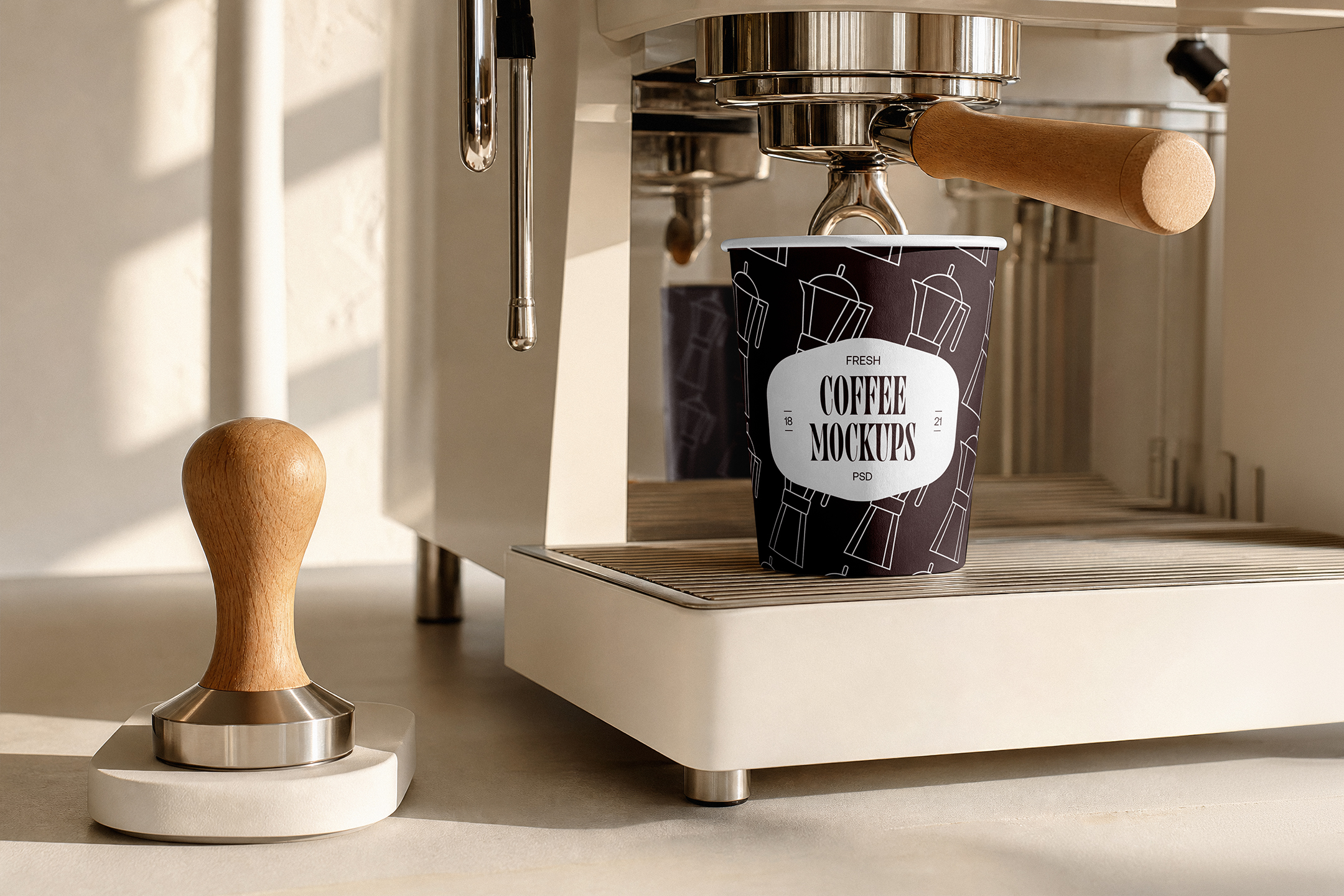 Paper-Coffee-Cup-Mockup-01-CMV2-A A dark paper coffee cup sitting directly under the group head of a modern cream-colored espresso machine, next to a wooden tamper.