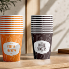 Two neatly stacked piles of paper coffee cups—one orange and one dark brown—sitting side by side on a wooden countertop.