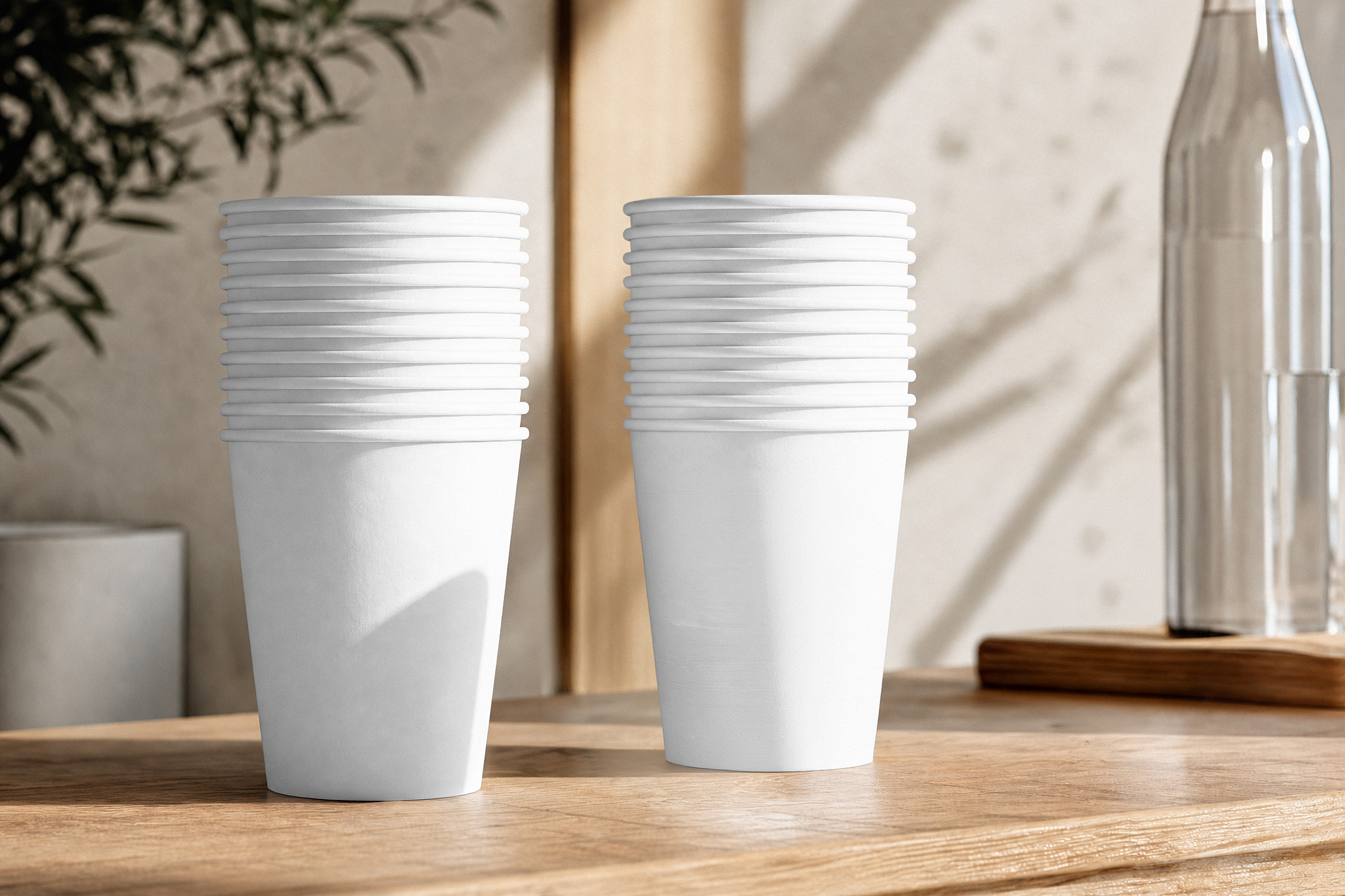 Two tall stacks of blank white paper coffee cups standing side-by-side on a wooden counter in a bright, sunlit room.