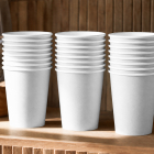 Three stacks of blank white paper coffee cups lined up on a wooden shelf against a slatted wooden wall.