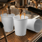 Fresh espresso pouring from a coffee machine group head into a blank white paper cup on a stainless steel drip tray.