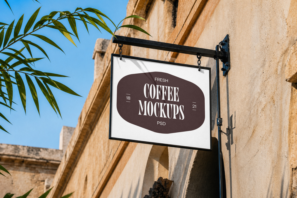 A hanging white outdoor store sign mounted on a textured stone building façade under a clear blue sky, displaying a dark brown logo badge.
