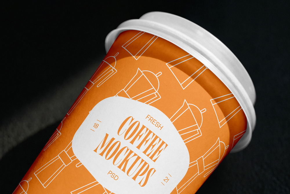 Close-up angled view of an orange paper coffee cup with a white lid, featuring a Moka pot pattern and a white badge reading "Fresh Coffee Mockups".