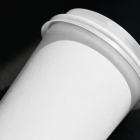Close-up view of a blank white paper coffee cup with a lid resting at an angle on a dark, textured surface.
