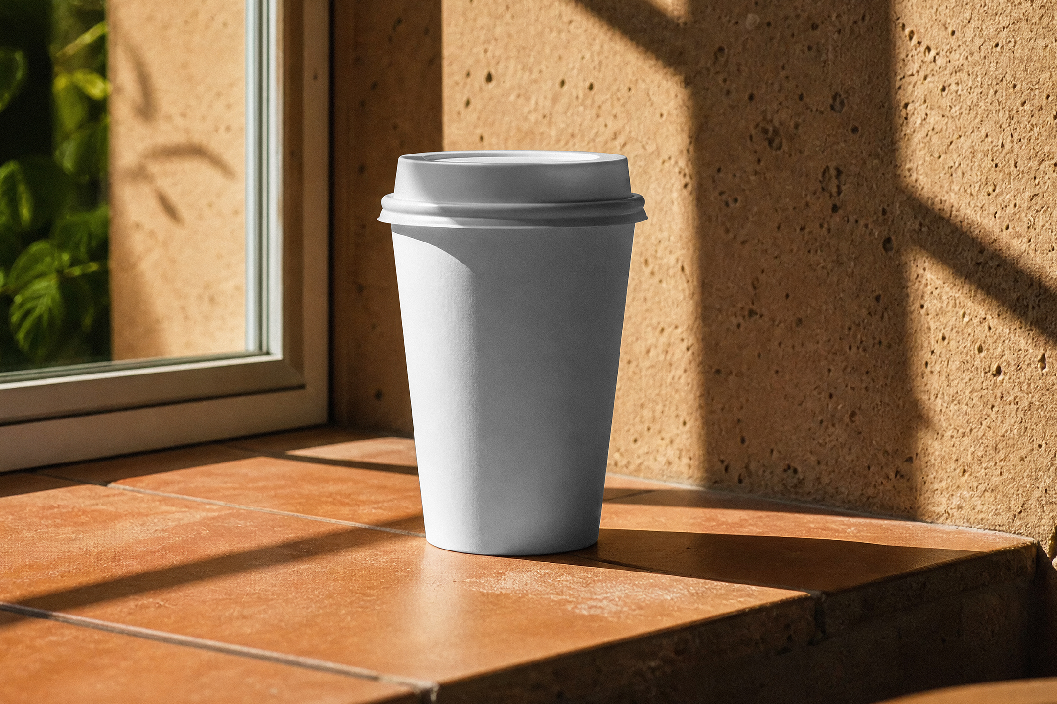 A blank white paper coffee cup with a lid standing on a terracotta tiled windowsill in warm, direct sunlight.