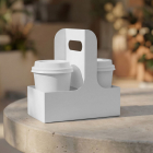 Two white paper takeaway coffee cups with lids inside a blank white cardboard cup holder carrier on a round stone table outdoors.