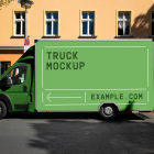 Side view of a green commercial box truck mockup parked on an urban street in front of a yellow residential building.