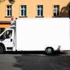 Side view of a modern white box delivery truck parked on an urban street in front of a warm orange building with windows.