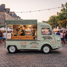 Vintage mint green food truck mockup with an open hatch serving coffee and teas, set up at an outdoor evening festival with overhead string lights and crowds of people.