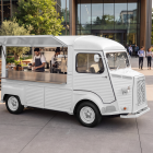 Vintage white Citroen HY coffee truck mockup with open hatch parked in a modern courtyard next to outdoor seating.