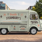 Side view of a vintage mint green food truck mockup with a closed hatch, parked on a paved walkway in a modern urban park setting.