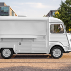 Vintage white Citroen HY food truck mockup with closed hatch parked on a paved walkway near an urban park.