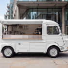 Vintage white Citroen HY coffee truck mockup with open hatch parked on a paved plaza near modern office buildings.