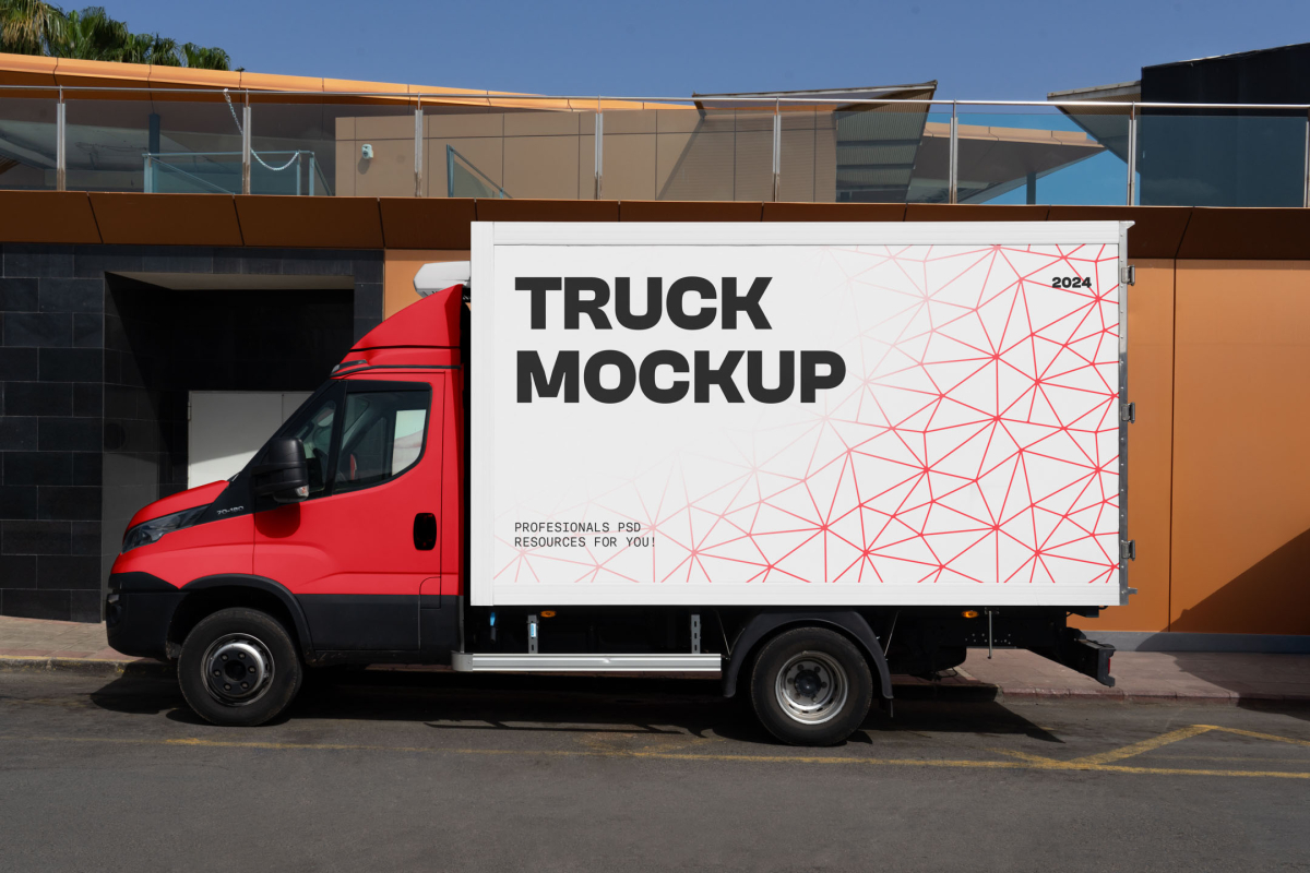 Side view of a red delivery truck with a white cargo box featuring a red geometric pattern, parked in front of a modern building.