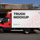 Side view of a red delivery truck with a white cargo box featuring a red geometric pattern, parked in front of a modern building.