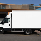 Side view profile of a white commercial cargo box truck parked against a modern building with metallic and orange panels.