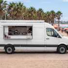 White van food truck mockup with open service window parked on a wooden promenade by a sunny beach.