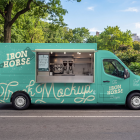 Side profile of a turquoise coffee and burger food truck mockup with an open hatch displaying espresso equipment, parked on an empty street lined with lush green trees.