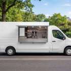 Side view of a white mobile coffee van mockup with open hatch parked along a park road.