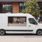 Side view of a white food truck mockup with open hatch and chef preparing food near an outdoor cafe terrace.