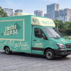 Side view of a turquoise food truck mockup with a closed hatch parked on a paved pedestrian plaza surrounded by trees and modern office buildings.