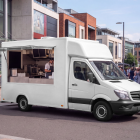White food truck mockup with open service window parked along a paved pedestrian street near shop fronts.