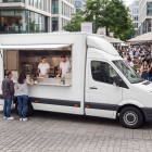 White van food truck mockup with open hatch and chefs serving customers in a busy pedestrian precinct.