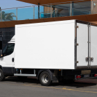 Rear three-quarter view of a white delivery box truck with double back doors parked on an asphalt street near a modern structure.
