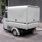 Rear angle view of a vintage off-white Piaggio Ape three-wheeled cargo truck parked on a paved pedestrian walkway.