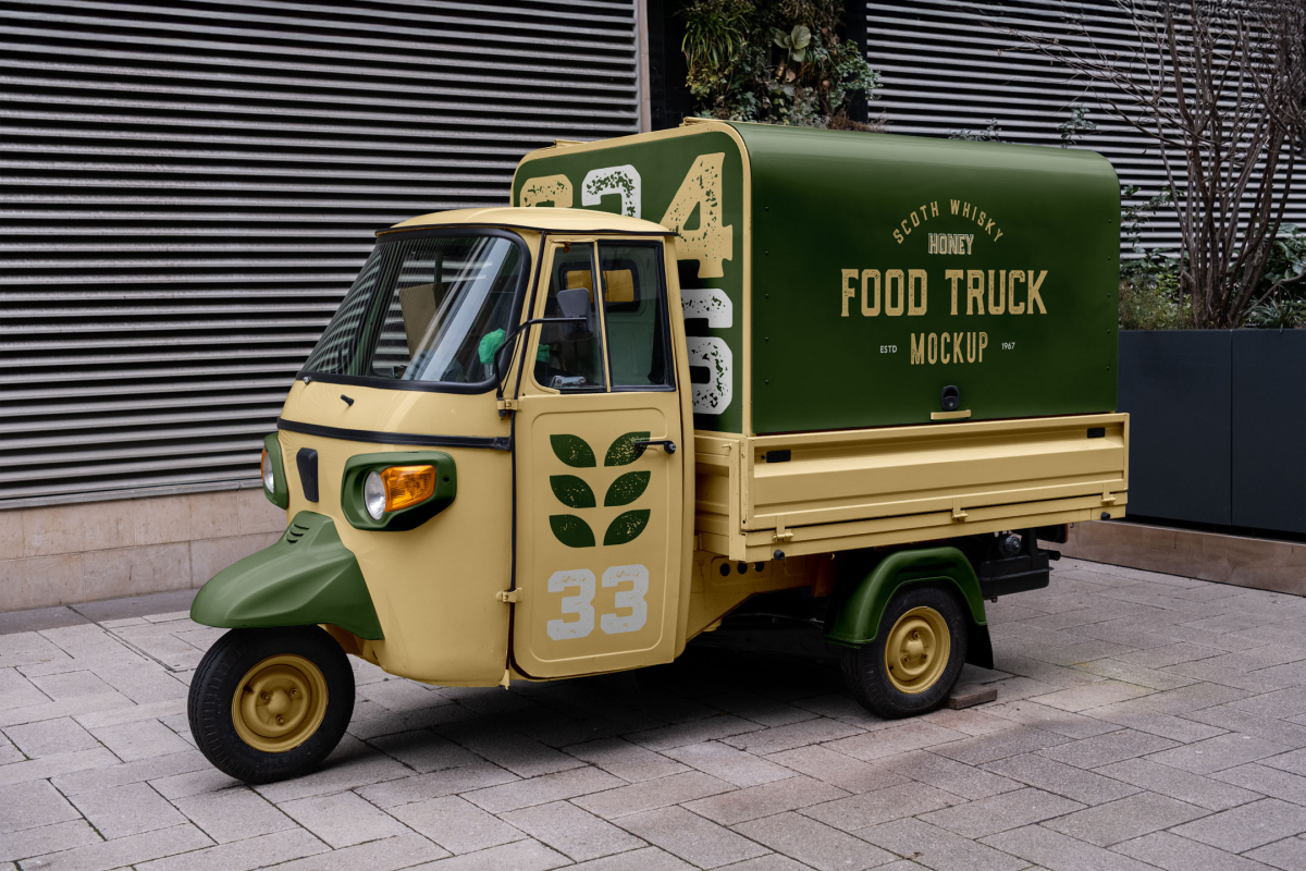 Three-quarter view of a vintage yellow and dark green Piaggio Ape food truck mockup parked on a paved sidewalk.