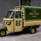 Three-quarter view of a vintage yellow and dark green Piaggio Ape food truck mockup parked on a paved sidewalk.