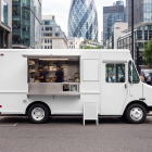White step van food truck mockup with open hatch parked near modern office buildings in a financial district.