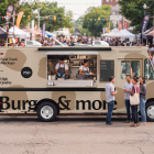 Beige food truck mockup with an open service hatch parked at a busy outdoor street festival, with staff working inside and customers standing in front of the vehicle.