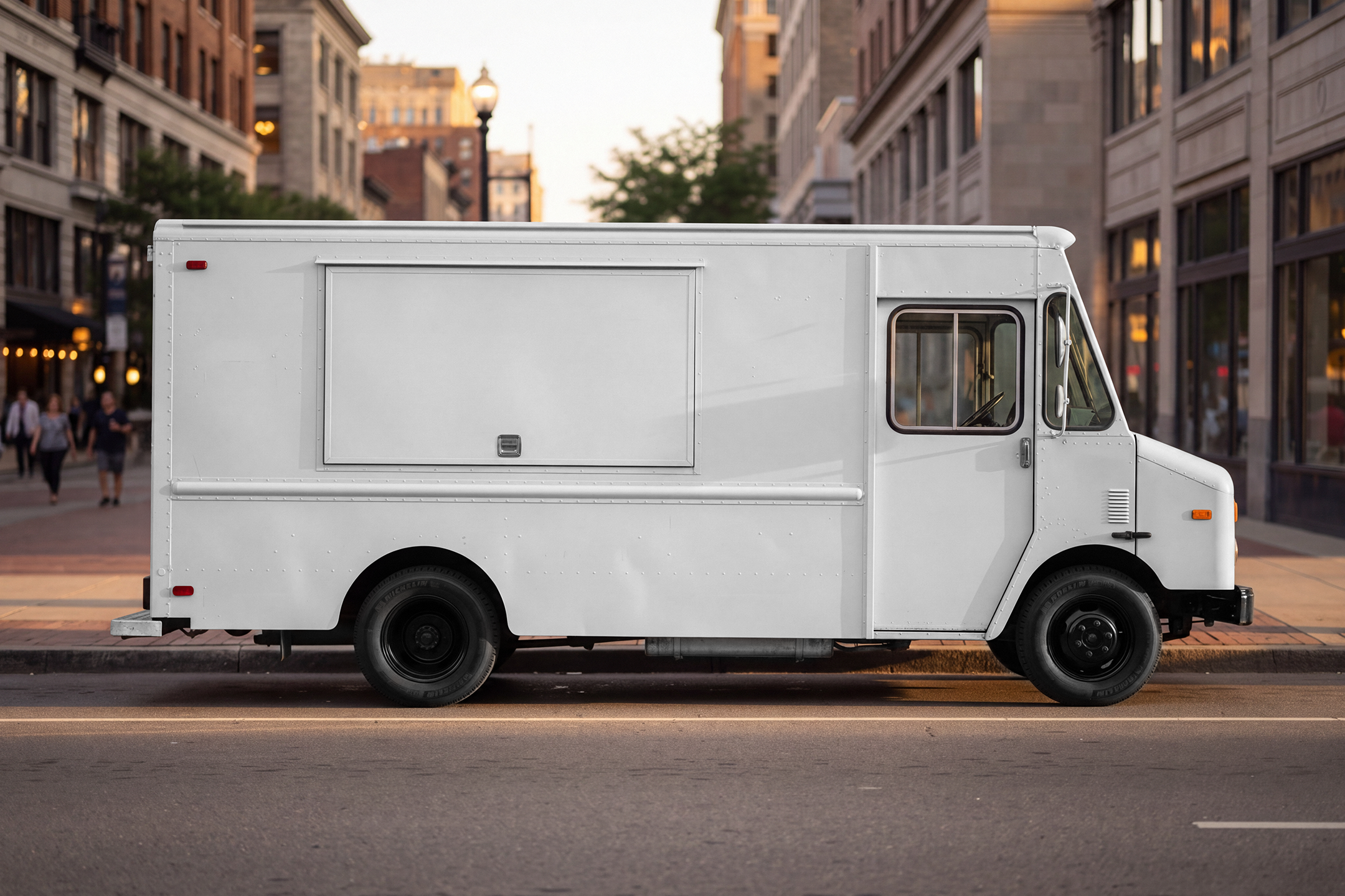 Side profile of a white step van food truck mockup with closed hatch parked along a city curb during golden hour.