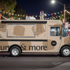 Nighttime side view of a beige food truck mockup parked at a lively outdoor night market decorated with glowing festoon lights.