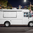 Side profile of a white step van food truck mockup with closed hatch parked at a night festival with string lights.