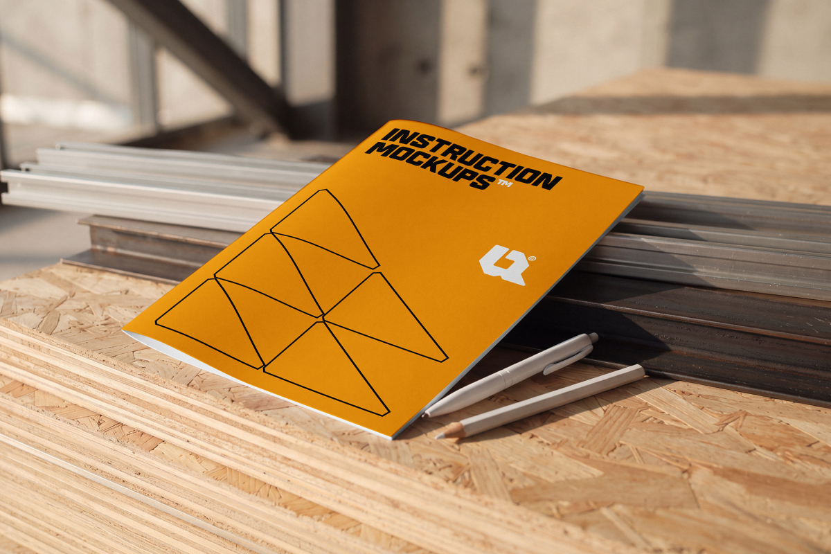 Orange instruction booklet resting on OSB boards beside two pens at a job site.