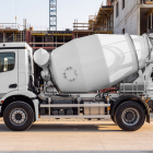 Side view of a white concrete mixer truck parked in front of a building under construction.