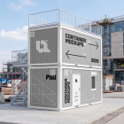 Perspective view of stacked grey modular containers with an external metal staircase at a construction site.