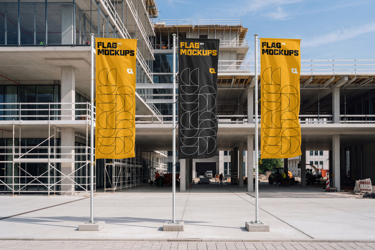 Three vertical promotional flags standing on concrete pedestals in front of a multi-story building under construction.