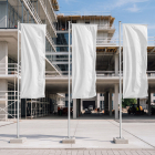 Three tall white vertical flags on concrete bases are set up in front of a modern building under construction.