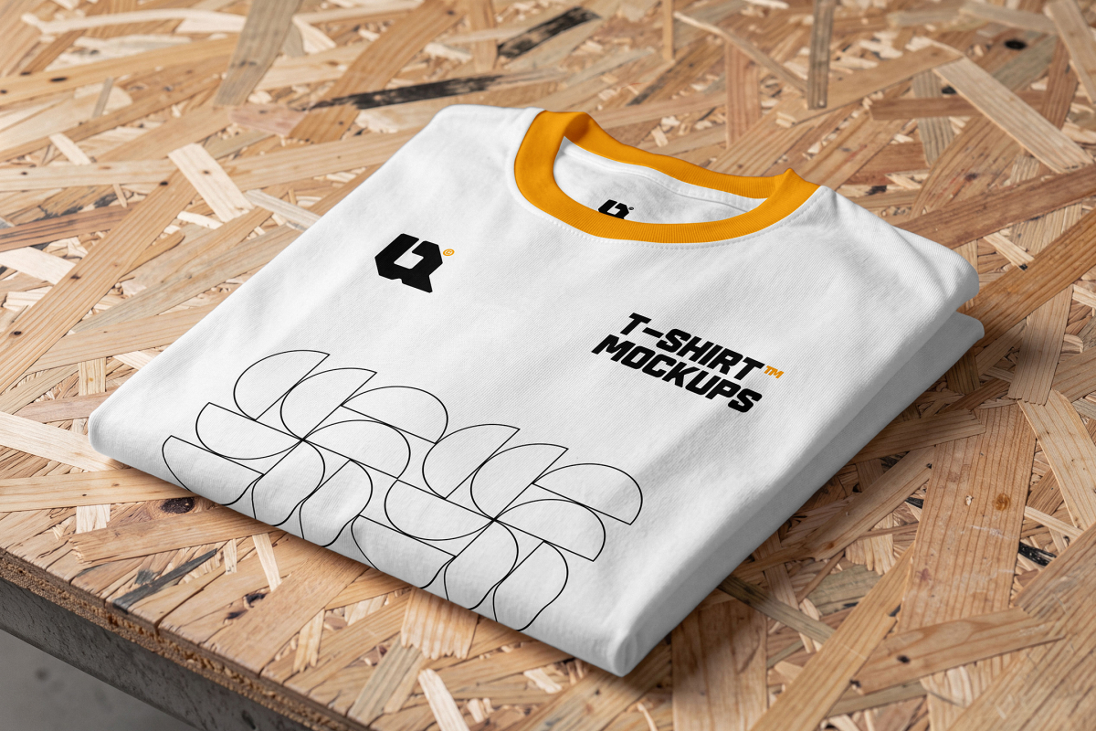 A folded white t-shirt with a yellow crew neck collar and printed graphics lying on an OSB board.