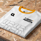 A folded white t-shirt with a yellow crew neck collar and printed graphics lying on an OSB board.