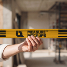 A person holding a yellow folded wooden ruler horizontally in front of an indoor construction site background.