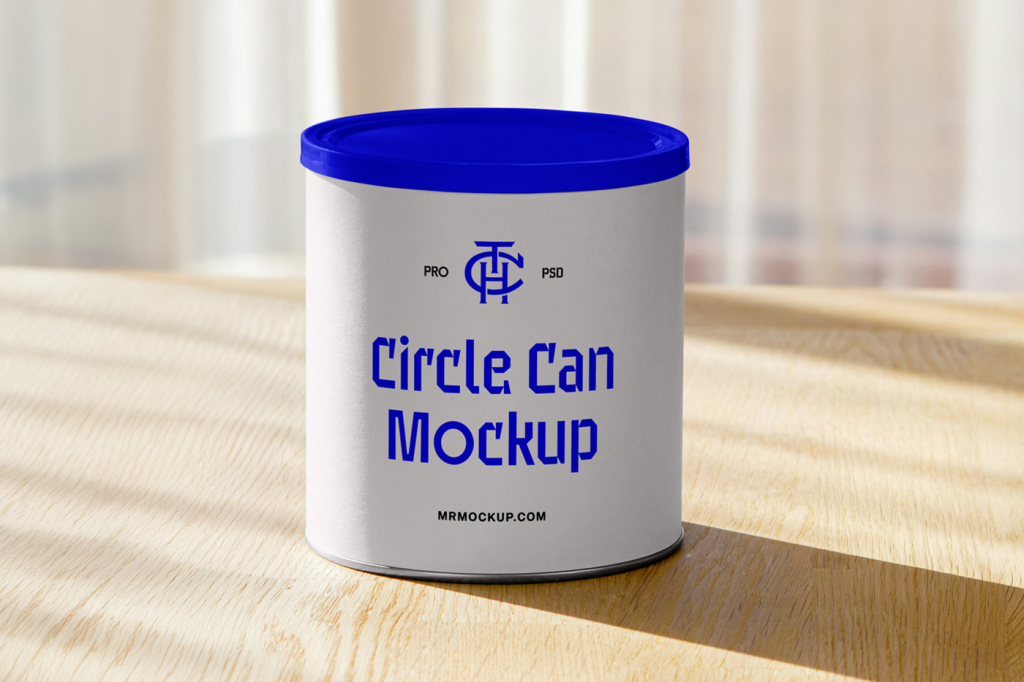 A plain white cylindrical can mockup standing upright on a light wooden table, illuminated by soft sunlight casting a shadow in the foreground with a blurred background. Free Circle Can Mockup