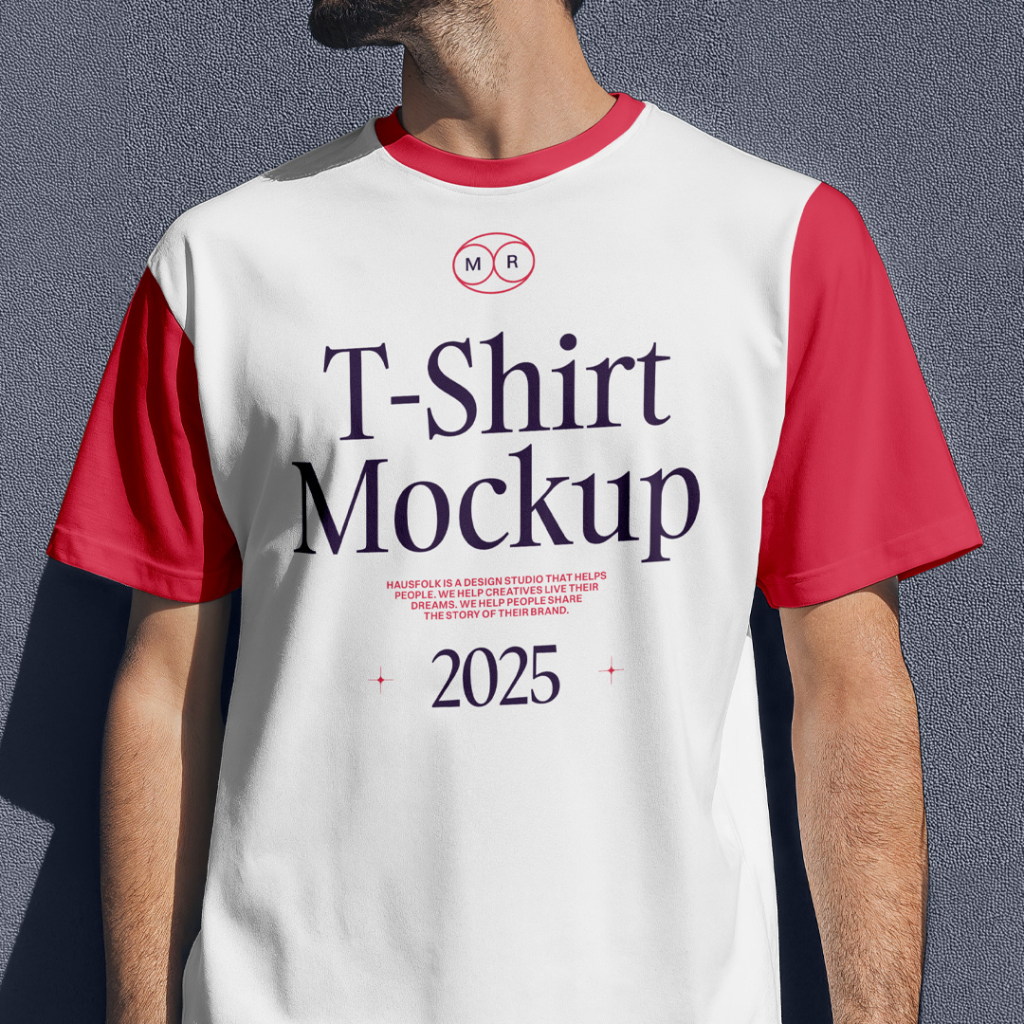A front-view apparel mockup featuring a man standing outdoors against a dark grey textured concrete wall in natural sunlight. He wears a plain, blank white crewneck t-shirt with loose short sleeves, showcasing realistic fabric folds and shadows ideal for apparel brand designs. Free Front View Men Wearing T-Shirt Mockup