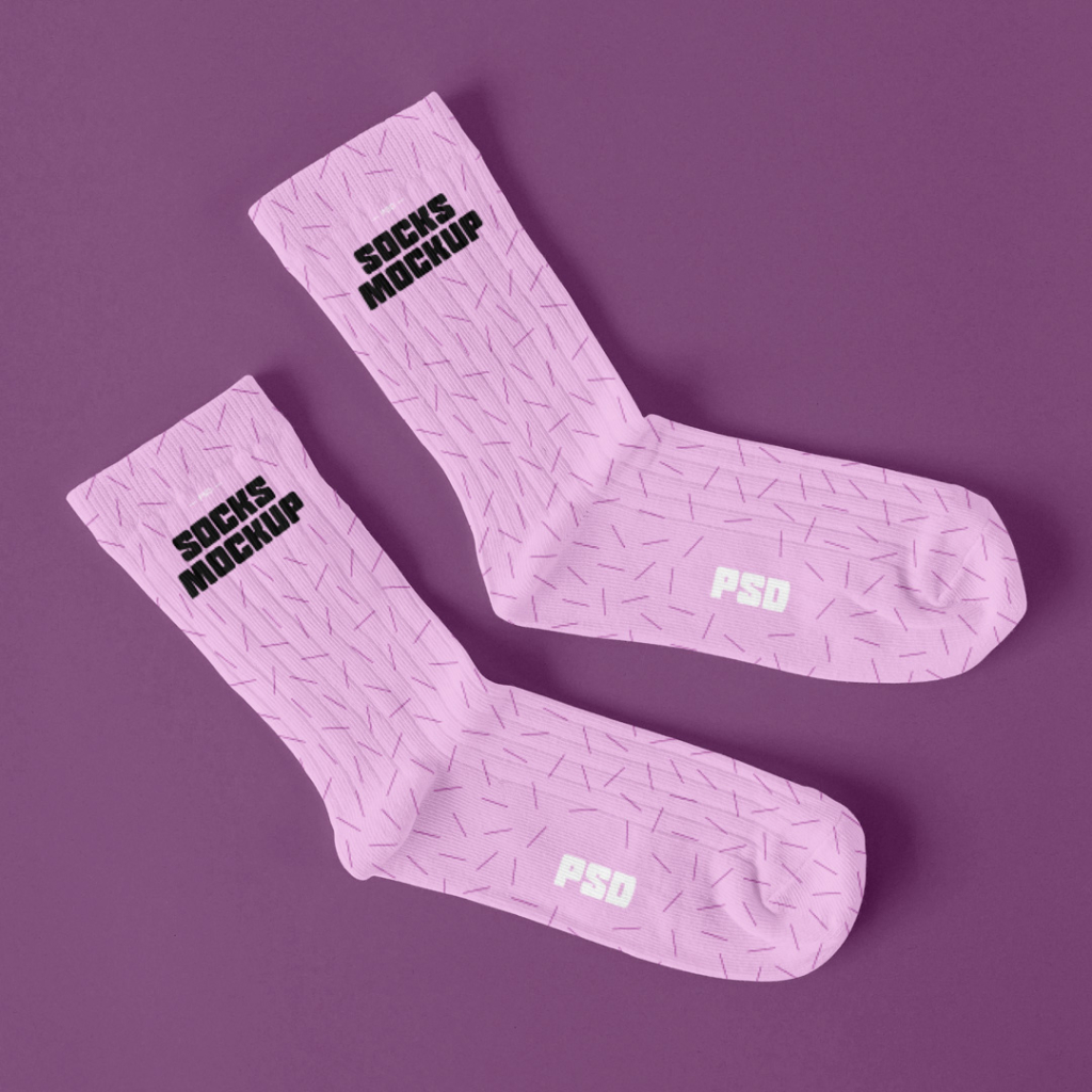A high-angle flat lay mockup featuring a pair of blank white crew socks made of ribbed cotton knit fabric, placed side-by-side on a seamless, light off-white background with soft, natural shadows. Free Laying Pair of Socks Mockup